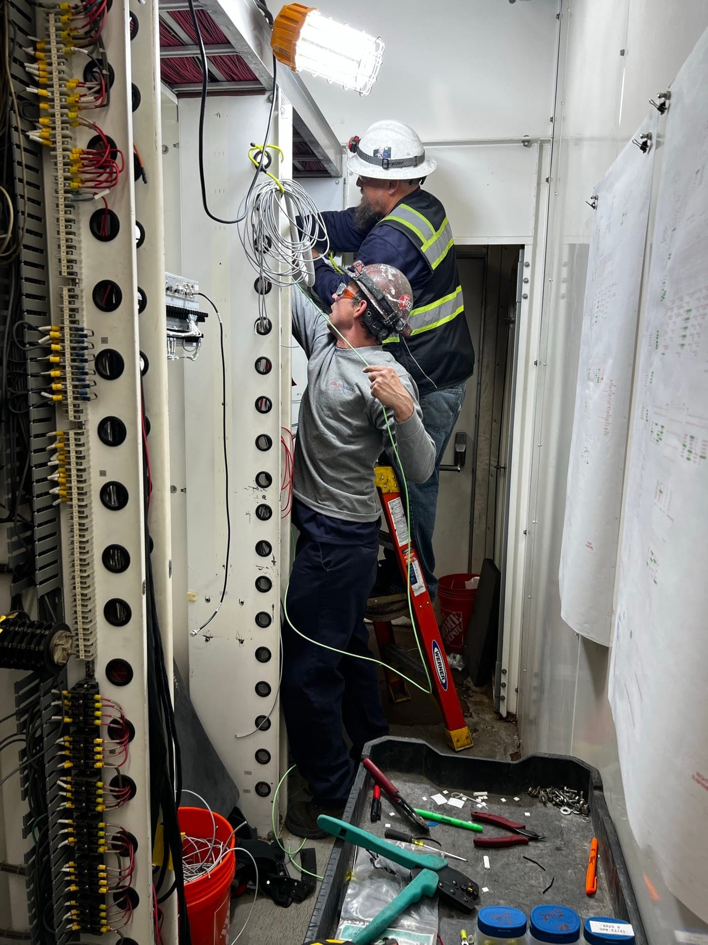Two Electrisource electricians wiring control cabinets from engineered drawings